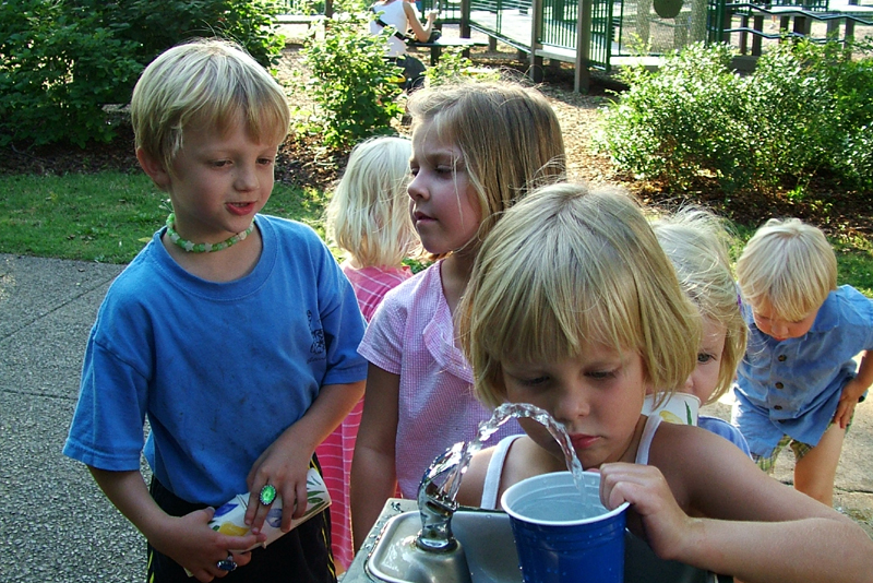 children drinking from a water cooler and fountain