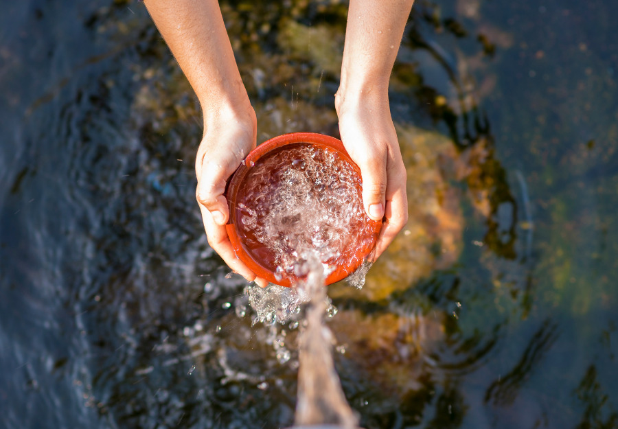 Hands filling a dish with fresh water from a spring - the best quality drinking water