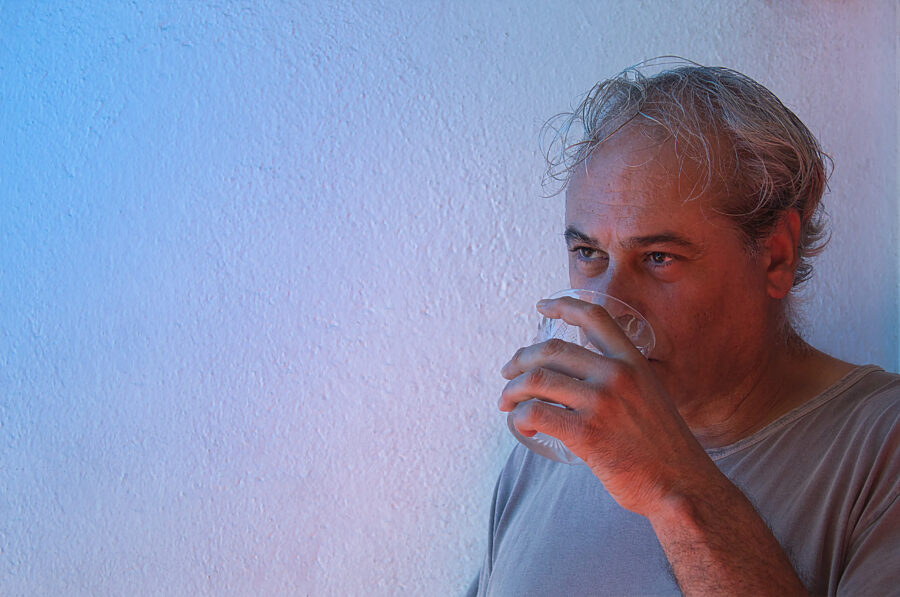 Middle aged man in gray shirt drinking water against wall